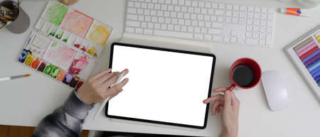 Overhead shot of female artist working with mock-up tablet, painting tools and drinking coffee on office deskの写真素材
