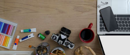 Top view of wooden worktable with laptop, smartphone, camera, coffee mug, painting tools and copy spaceの写真素材