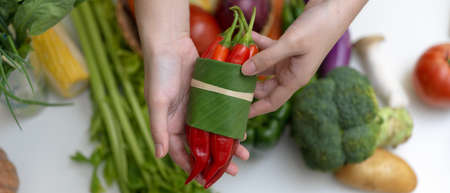Close up view of hands holding red chili pepper while standing at table with other fresh farm vegetablesの写真素材