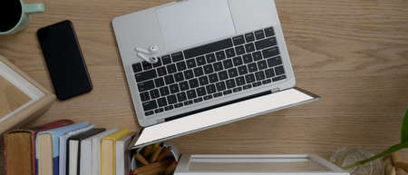Top view of wooden worktable with mock-up laptop, smartphone, books, stationery and decoration
