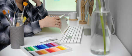 Side view of female artist working with  tablet, computer and painting tools on white office deskの写真素材