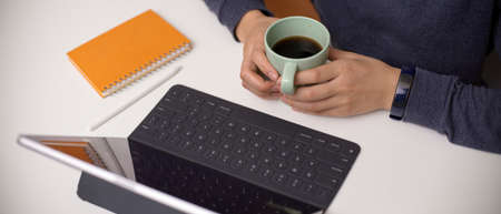 Overhead shot of female employee holding coffee cup while reading informations on digital tablet on white deskの写真素材