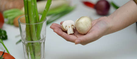 Close up view of hand holding white button mushrooms while standing at table with other fresh farm vegetablesの写真素材