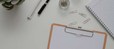 Top view of white office desk with paper on clipboard, stationery, schedule book and other office suppliesの写真素材