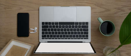 Overhead shot of wooden office desk with mock-up laptop, smartphone, coffee mug and decorations