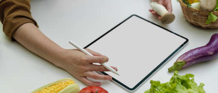 Close up view of female cook online ordering ingredients on mock-up tablet at kitchen room 