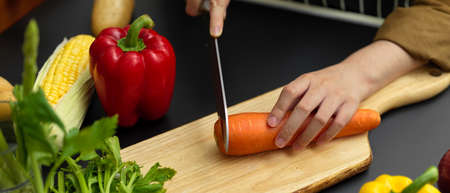 Close up view of female cook slicing fresh carrot on chopping block at dark modern kitchenの写真素材