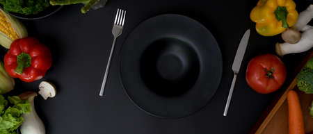 Top view of dark kitchen table with dinning set and fresh vegetables ingredientsの写真素材
