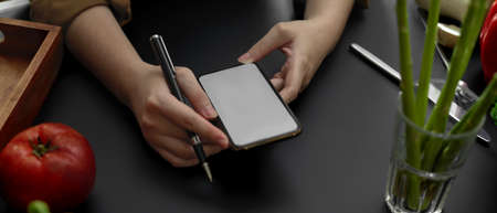 Close up view of female student using mock-up smartphone on black kitchen table in cooking class