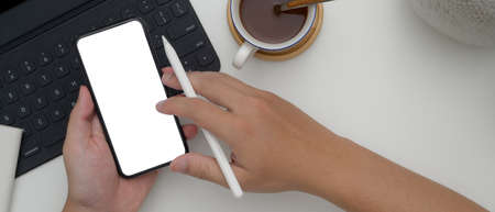 Overhead shot of male entrepreneur using smartphone while working with digital tablet and hot cocoa...