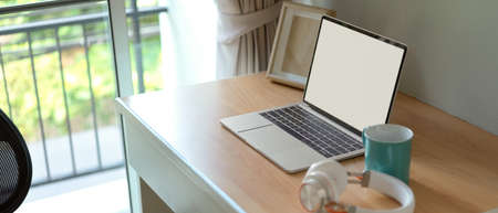 Side view of simple worktable with blank screen laptop, mock-up frame, headphone and mug on wooden table in bed room の写真素材