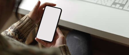 Close up view of female employee using mock-up smartphone to contact customer while sitting at...