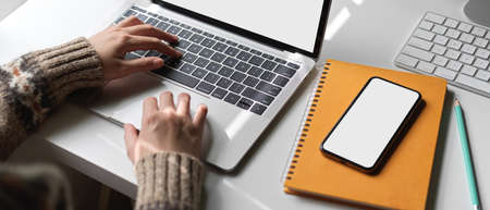 Close up view of female university student doing thesis with mock-up laptop, smartphone and...