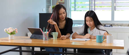 Cropped shot of female private tutor teaching her student with digital tablet and stationery on wooden table in living roomの写真素材