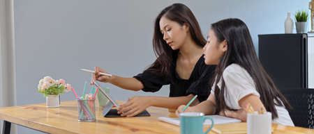 Side view of private tutor teaching her student with digital tablet and stationery on wooden table...