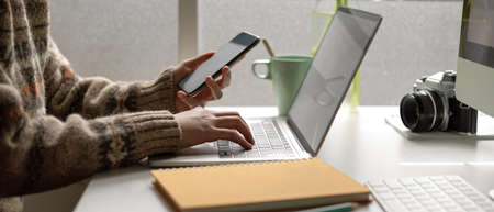 Side view of female university student looking information on smartphone while doing assignment on...
