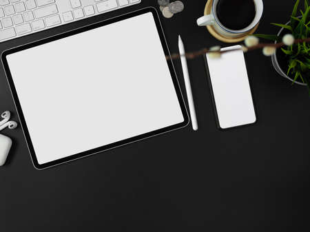Top view of blank screen smartphone, tablet, other supplies, decorations and copy space on dark modern worktableの写真素材