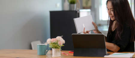 Cropped shot of female professor online teaching with digital tablet and notebook on wooden worktable in living room の写真素材