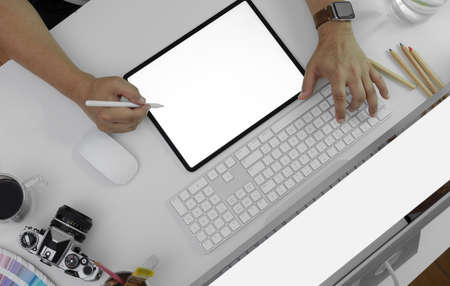 Overhead shot of male photographer using mock-up tablet on office desk with computer devices, camera...