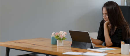Cropped shot of young female employee working from home with digital tablet and paperwork on wooden...