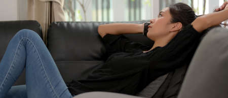 Close up view of young female lying relaxed on black sofa in living room and talking on the phone to...