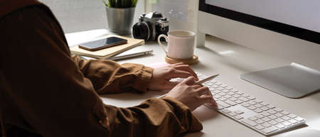 Cropped shot of female typing on computer keyboard on white office desk with smartphone and office...
