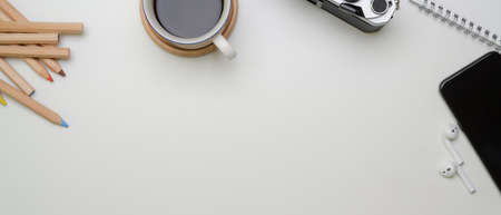 Top view of copy space on white worktable with coffee cup, camera, smartphone and stationery