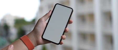 Close up view of hand holding blank screen smartphone while standing at balcony