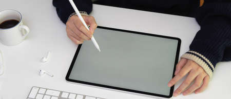 Close up view of female worker using mock-up tablet with stylus on white office desk with wireless...