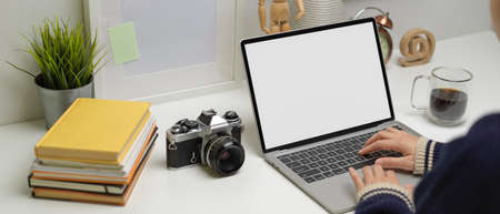 Cropped shot of female freelancer typing on mock-up laptop on home office desk with books, camera...
