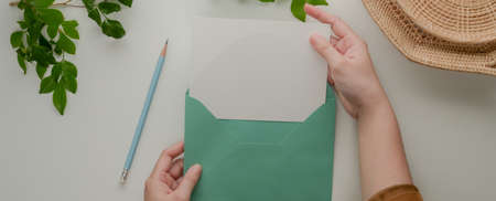 Overhead shot of female hands open mock-up greeting card with turquoise  envelope on table with...