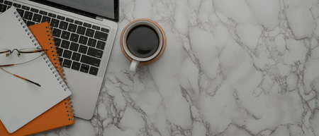 Top view of copy space on marble worktable with laptop, schedule books, coffee cup and glasses
