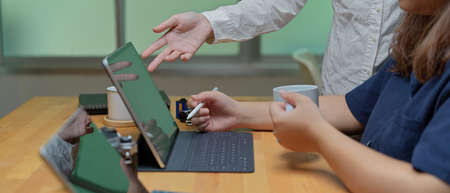 Side view of two female employees consulting on their project with digital tablet on wooden desk