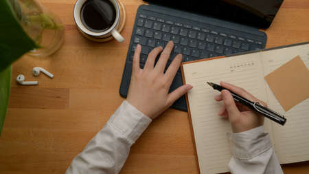 Overhead shot of female entrepreneur analysing business data on digital tablet and taking note on blank notebook on worktableの写真素材
