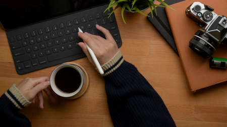 Overhead shot of female left hand holding coffee cup and right hand typing on tablet keyboard above...