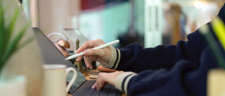 Side view of female hands using digital tablet with stylus pen on office desk with decoration and coffee cupの写真素材