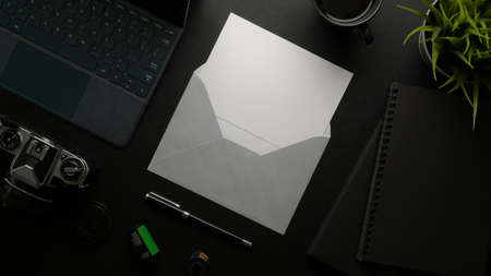 Overhead shot of mock-up greeting card with grey envelope on dark office desk with digital devices and office suppliesの写真素材