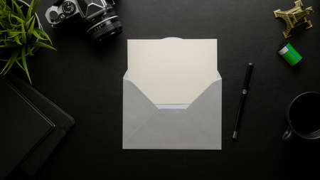 Overhead shot of open mock-up greeting card with grey envelope on dark office desk with digital camera and office suppliesの写真素材
