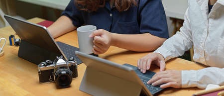 Cropped shot of two female partner working together with digital tablets and camera on wooden office...