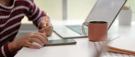 Side view of female working with mock up laptop, smartphone, notebook and coffee cup on white table