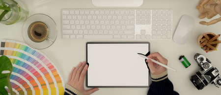 Top view of female designer working with mock up tablet, computer, camera and supplies on white desk