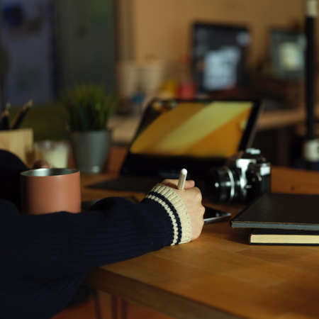 Cropped shot of female graphic designer working with digital tablet on rustic worktable with camera,...