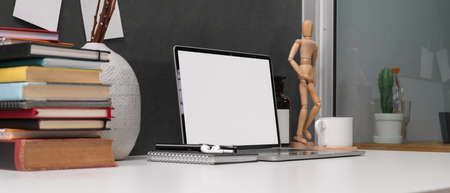 Cropped shot of study table with mock up laptop, stack of books and decorations on white desk