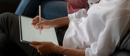 Close up view of female using mock up tablet with stylus on her lap while sitting near her friend on...