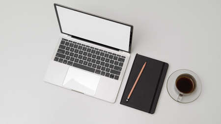 Top view of simple workspace with mock up laptop, schedule book, pencils and coffee cup on white deskの写真素材