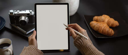 Close up view of female working with mock up tablet on worktable with camera, supplies, coffee cup and croissantsの写真素材