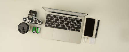 Top view of scene creator with laptop, smartphone, camera and supplies on white desk