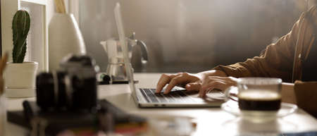 Side view of female photographer holding coffee cup while sitting at worktable with camera and...