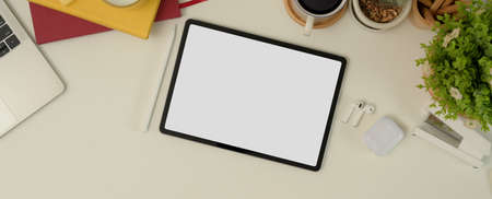 Top view of mock up tablet on working desk with notebooks, laptop, stationery, supplies and...