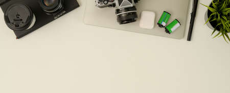 Top view of modern workspace with copy space, laptop, camera, lens, stationery and decoration on white tableの写真素材